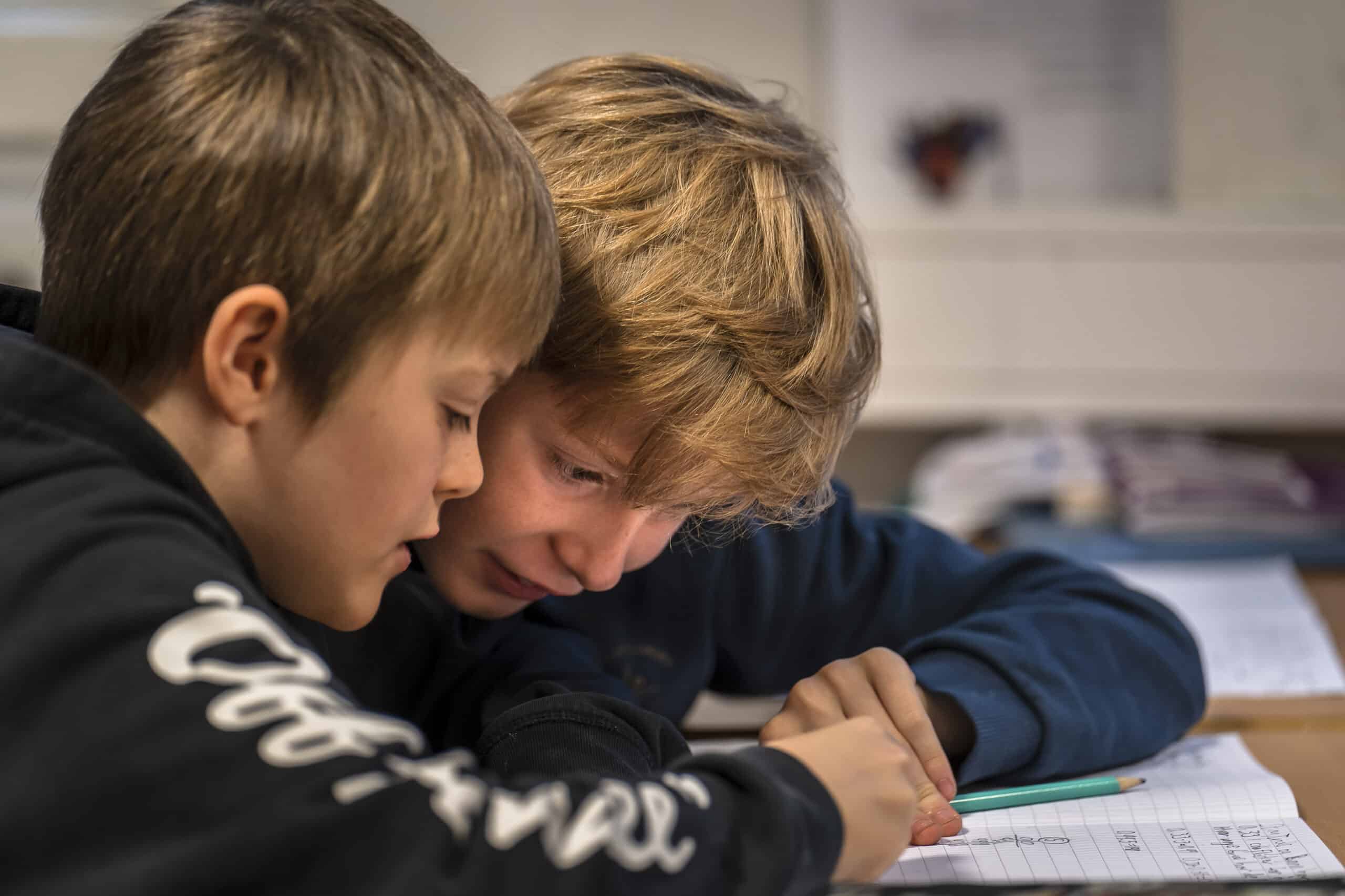 To elever som sitter konsentrert og bøyd over en matteoppgave på et ark. 